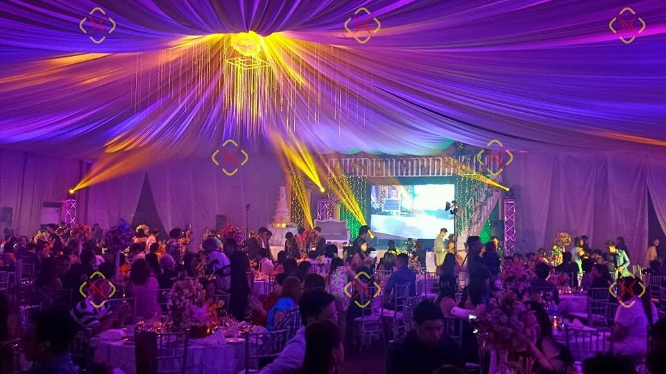 Large ballroom transformed by violet ceiling drapes, yellow moving beams, and immersive event lighting